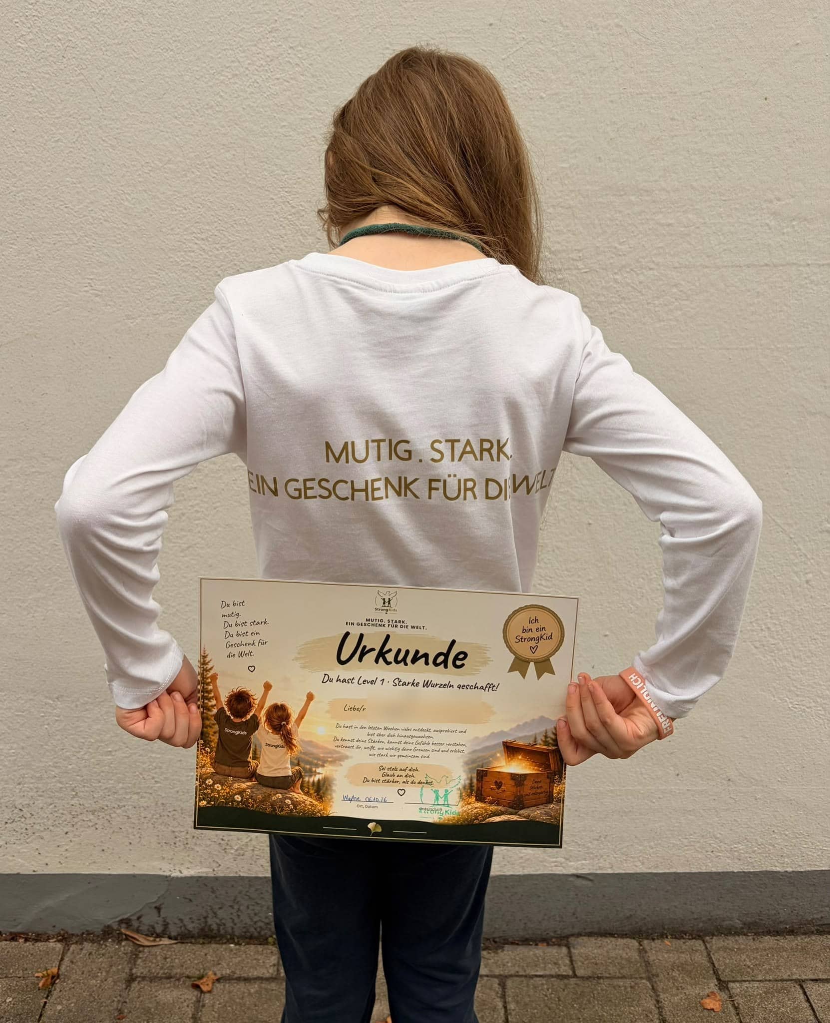 Kind von hinten im StrongKids-Shirt hält seine Urkunde für Level 1 „Starke Wurzeln“ hinter dem Rücken